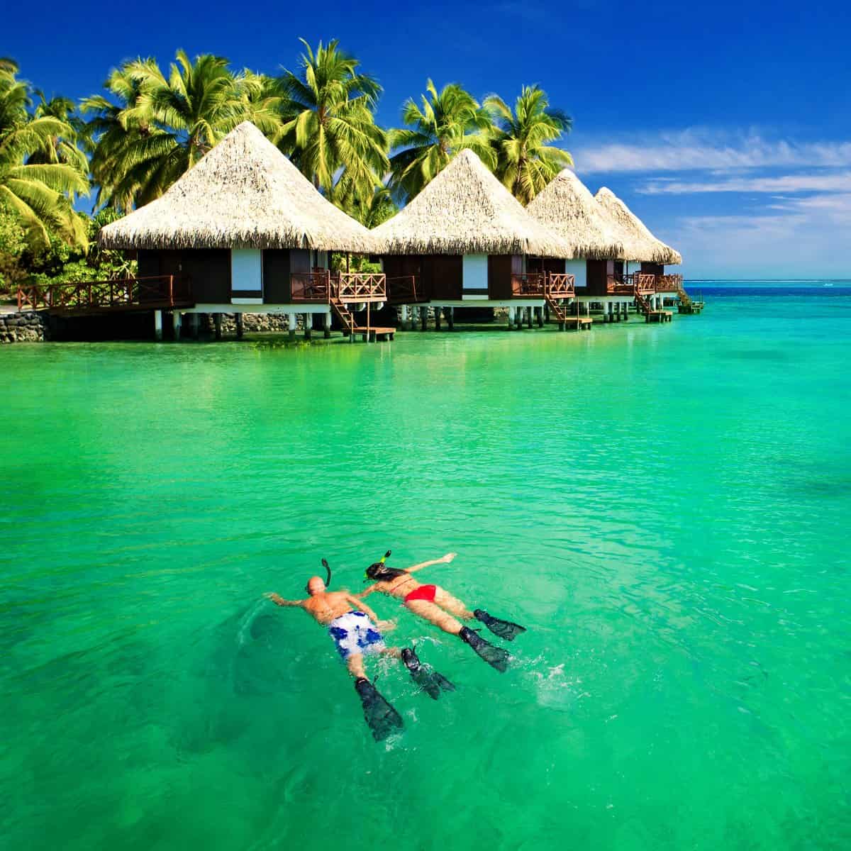 Couple swimming up to rooms over water with their Where To Enjoy employee and member benefits
